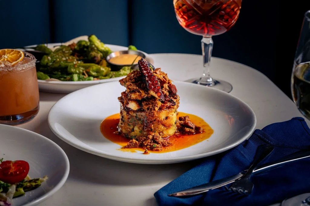 Meticulously plated cylindrical dish, cocktails, and sides on a restaurant table.