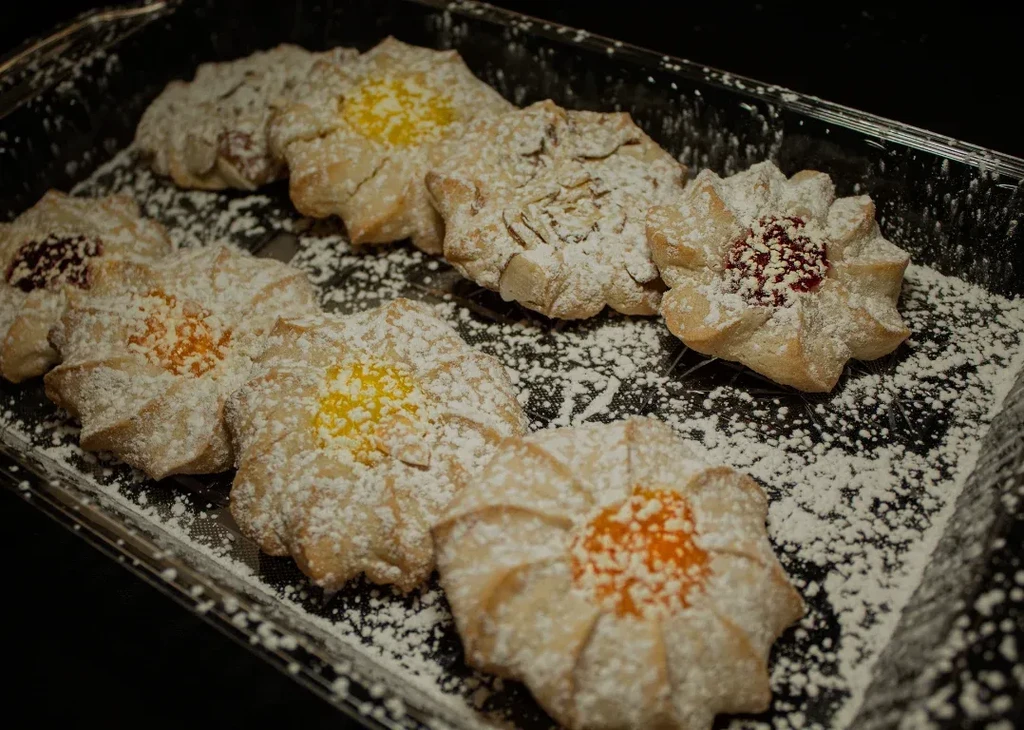 Close-up of flower-shaped cookies with colorful jam fillings and powdered sugar.