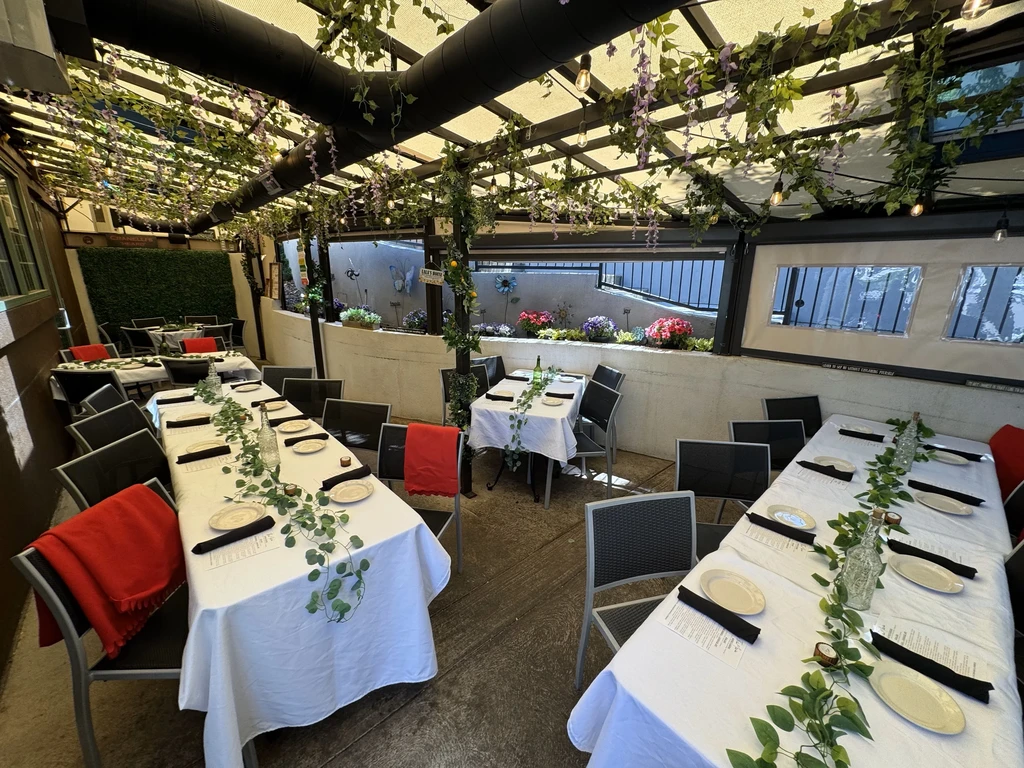 Lush outdoor restaurant patio with set tables, red blankets, and purple flowers.