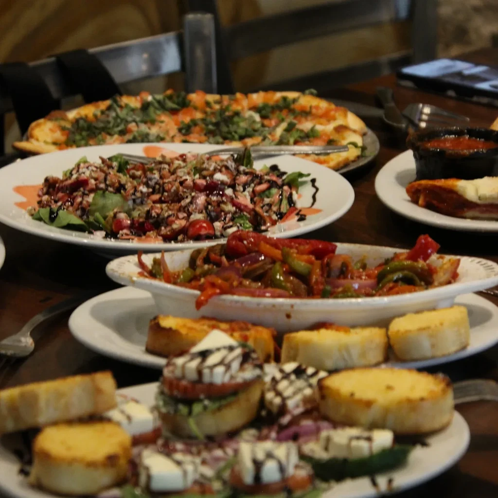 Bruschetta, pizza, salad, and vegetables on a wooden table.