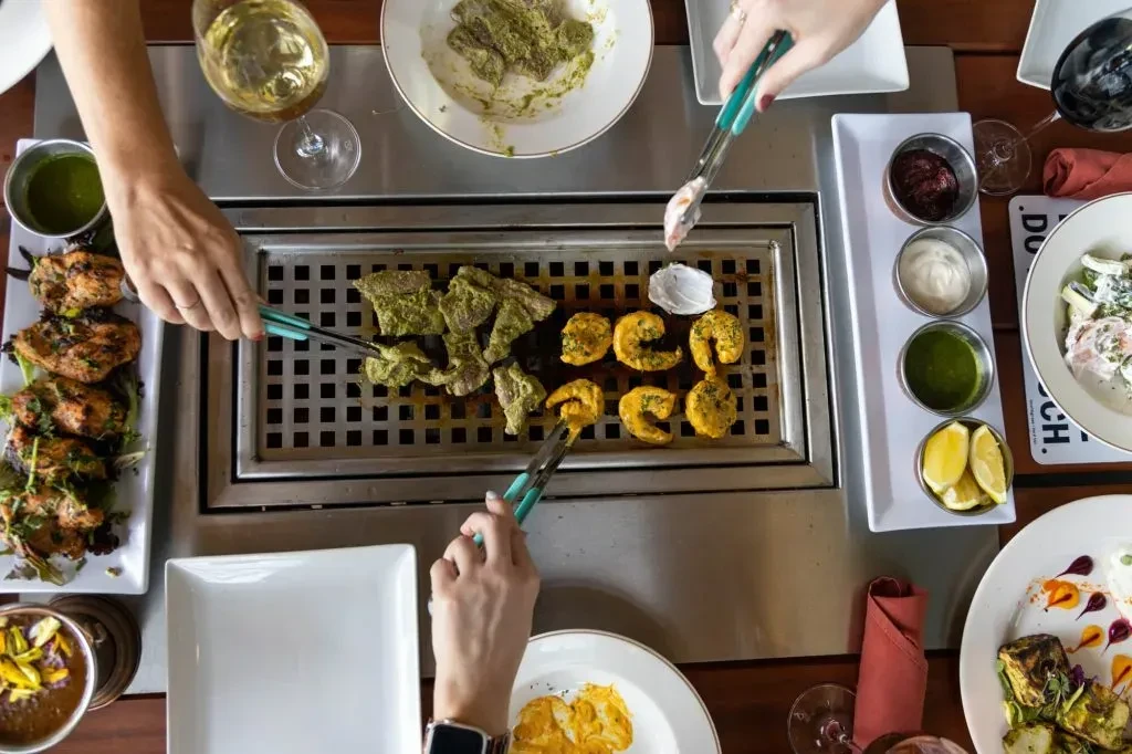 Restaurant tabletop grill cooking meat, seafood, and chicken, surrounded by condiments.