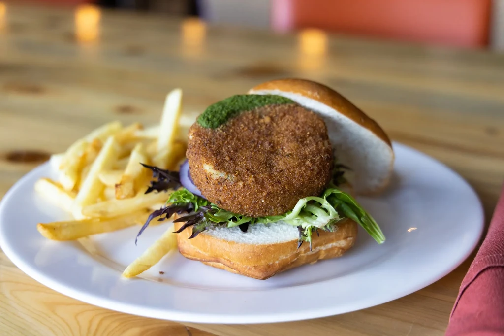 Close-up: Breaded patty burger with green sauce and fries.