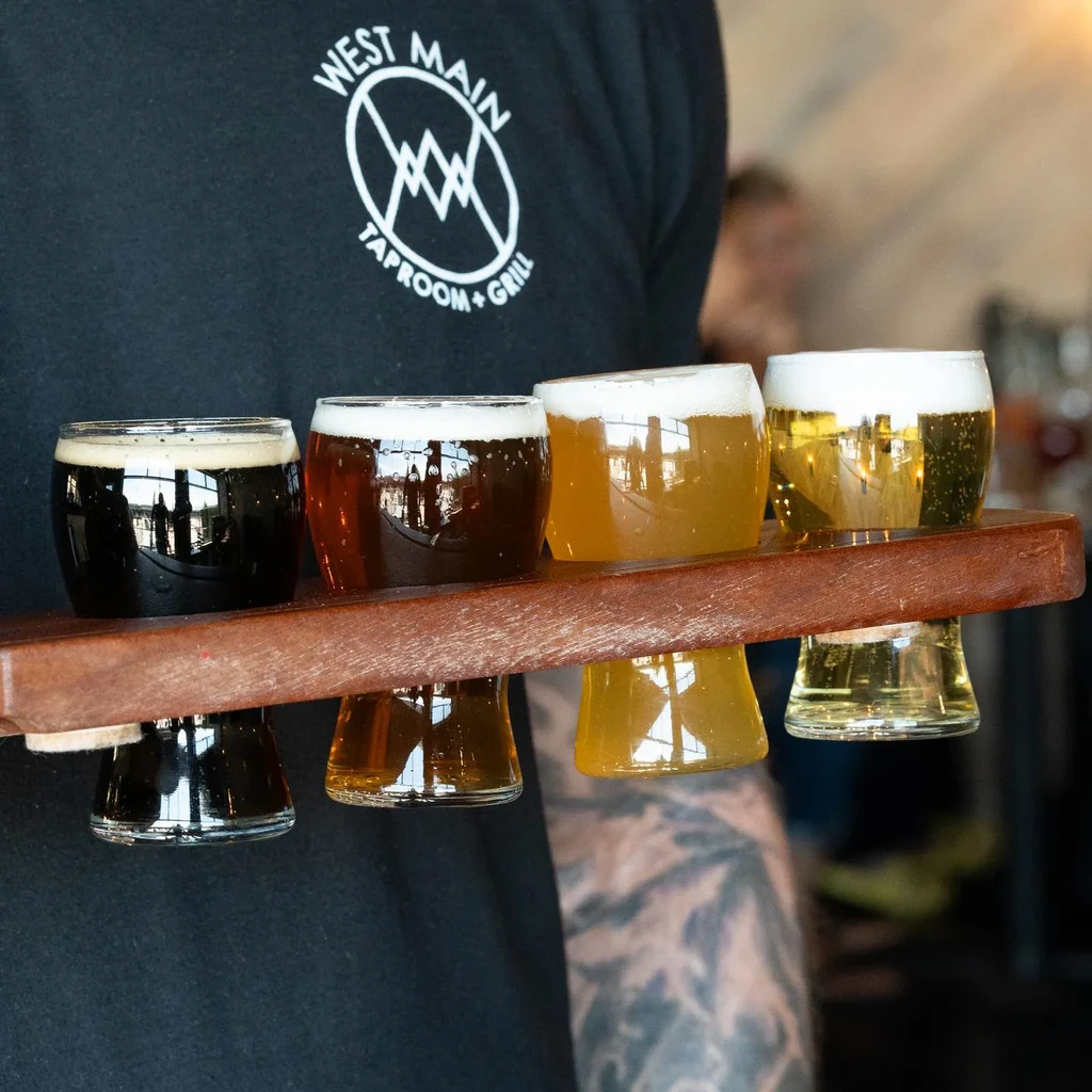 Person holds flight of four craft beers on a wooden paddle.