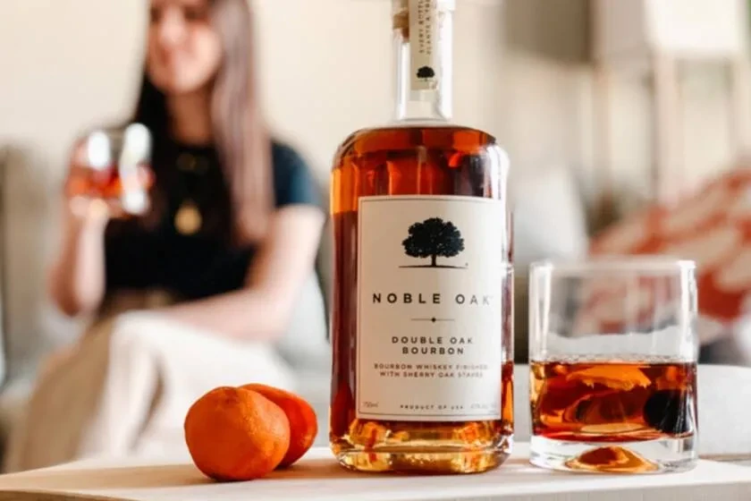 Noble Oak Double Oak Bourbon bottle, glass with ice, two oranges.
