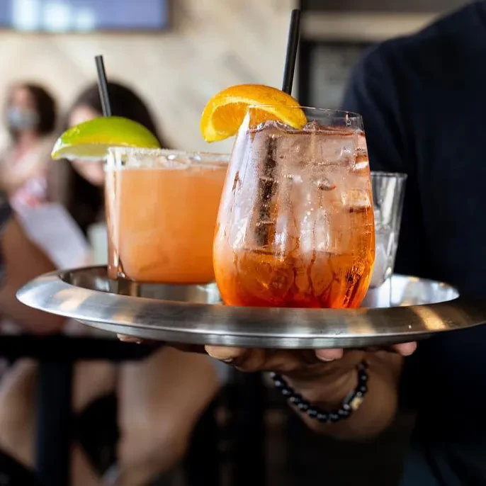 Two vibrant cocktails on a silver tray, held by a person.