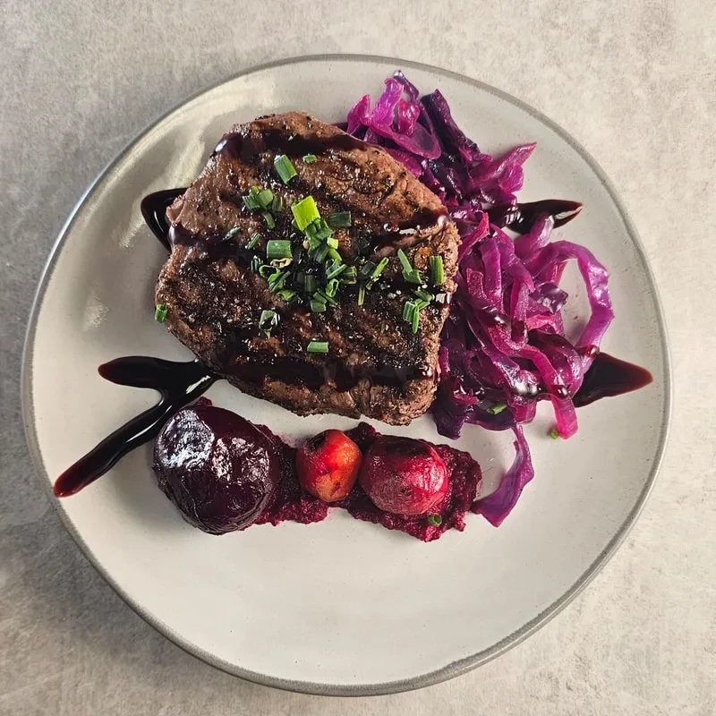 Plated steak, chives, dark sauce, red cabbage, and root vegetables.