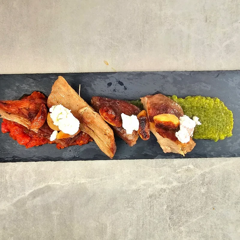 Roasted meat, bread, cheese, and sauces plated on dark slate.