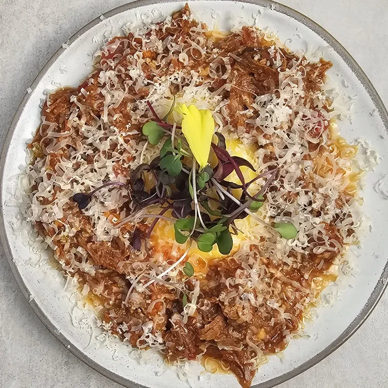 Close-up of ragu topped with cheese, yolk, and colorful microgreens.