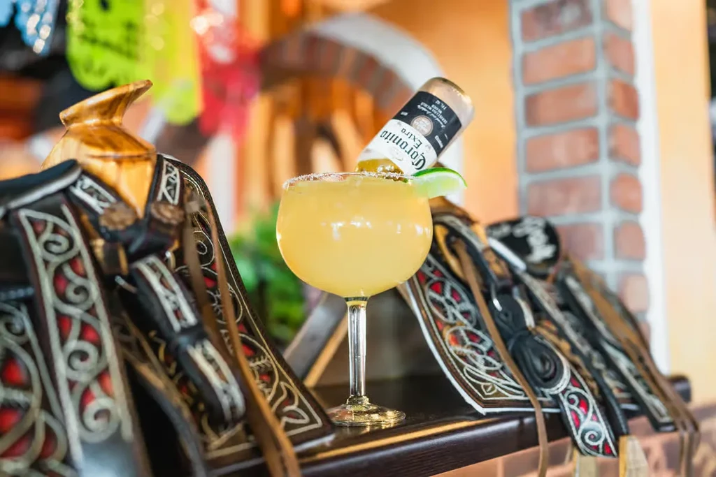 Margarita with inverted Corona bottle, framed by decorative leather saddles.