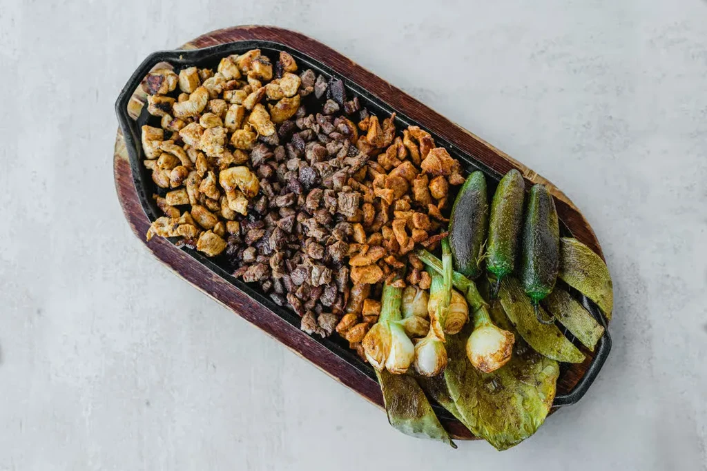 Top-down view of sizzling platter with mixed meats and grilled vegetables.