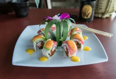Plated sushi rolls with avocado, pink fish, yellow sauce, and orchid.