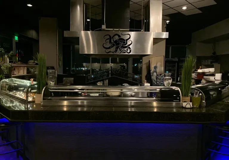 Dimly lit sushi bar counter featuring blue lights and an octopus hood.