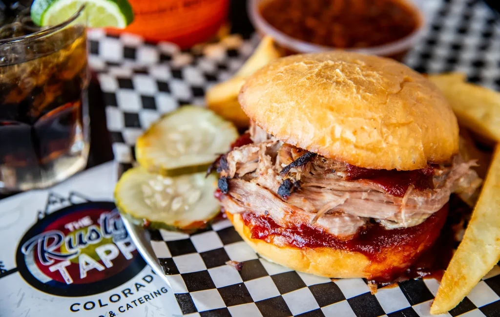 Pulled pork sandwich, fries, pickles, and Rusty Tapp logo.