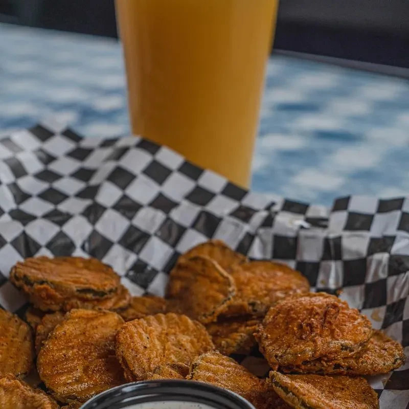 Golden fried pickles on checkered paper with dipping sauce and amber drink.