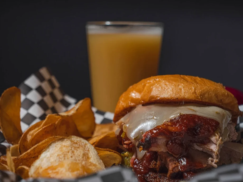 Cheesy pulled meat sandwich, crispy chips, and beverage in a basket.