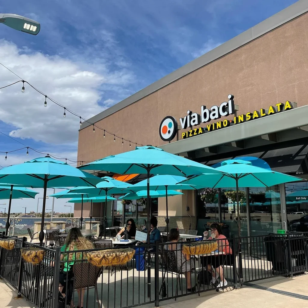 Via baci restaurant patio with teal umbrellas, string lights, and diners.