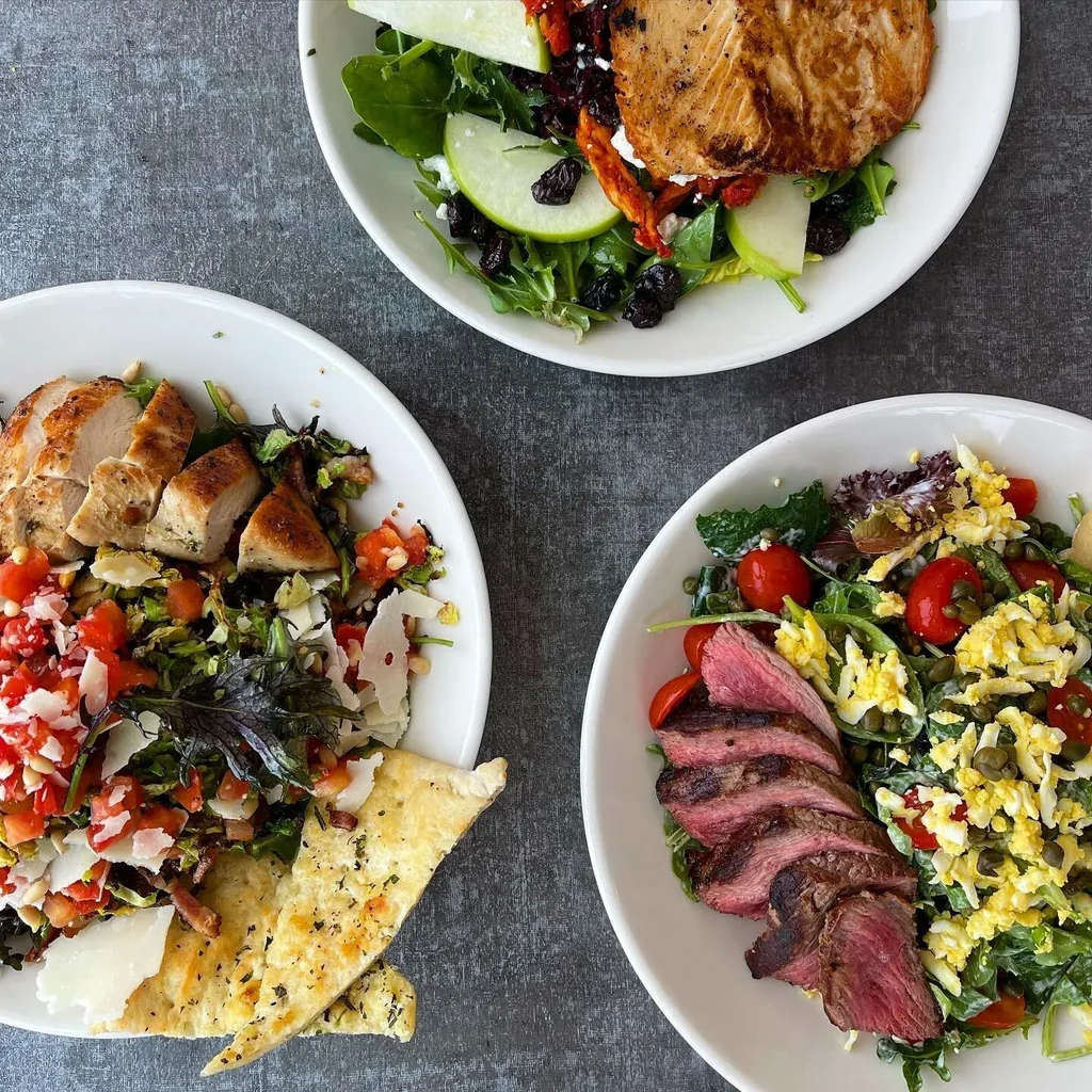Three overhead salad bowls with salmon, chicken, and steak.