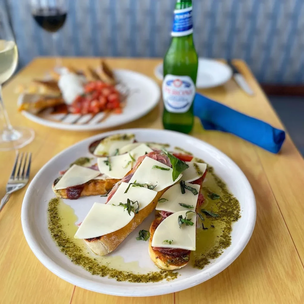 Three bruschetta with prosciutto, cheese, and basil, wine, and Peroni beer.
