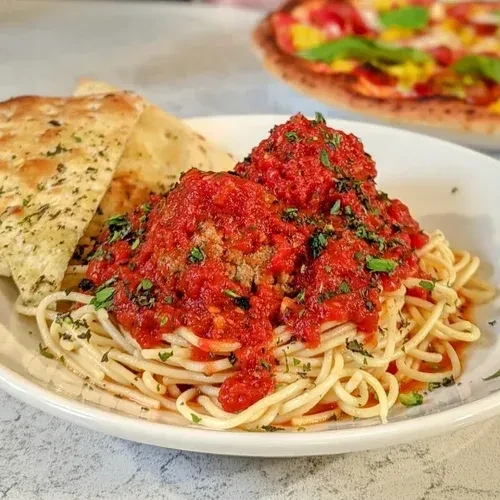 Spaghetti and meatballs, red sauce, herbs, flatbread; pizza in background.