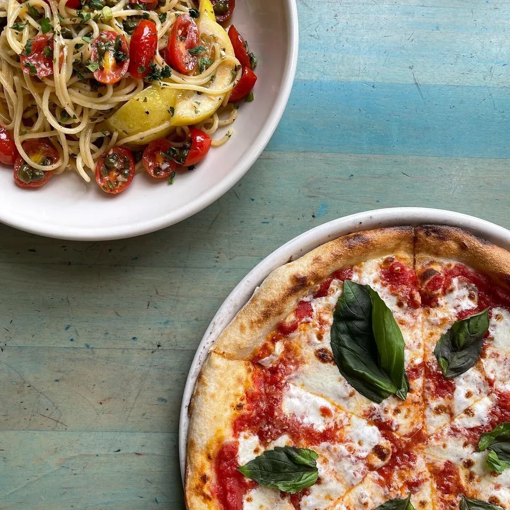 Spaghetti with lemon and Margherita pizza on a blue wooden table.