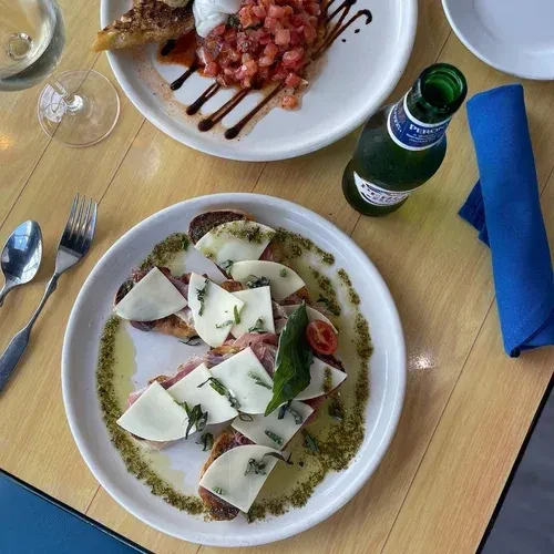Overhead: Two plates of bruschetta, caprese, wine, and beer on a wood table.