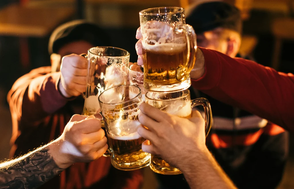 Four hands clinking beer mugs filled with amber liquid.