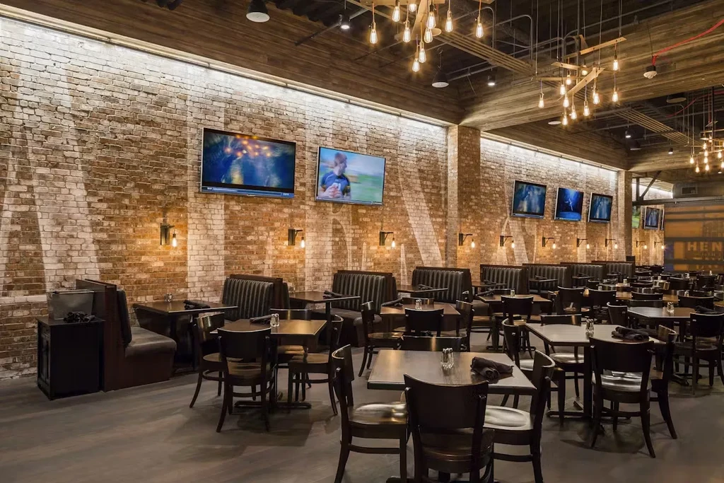 Empty restaurant interior with brick walls, industrial lighting, and many TVs.