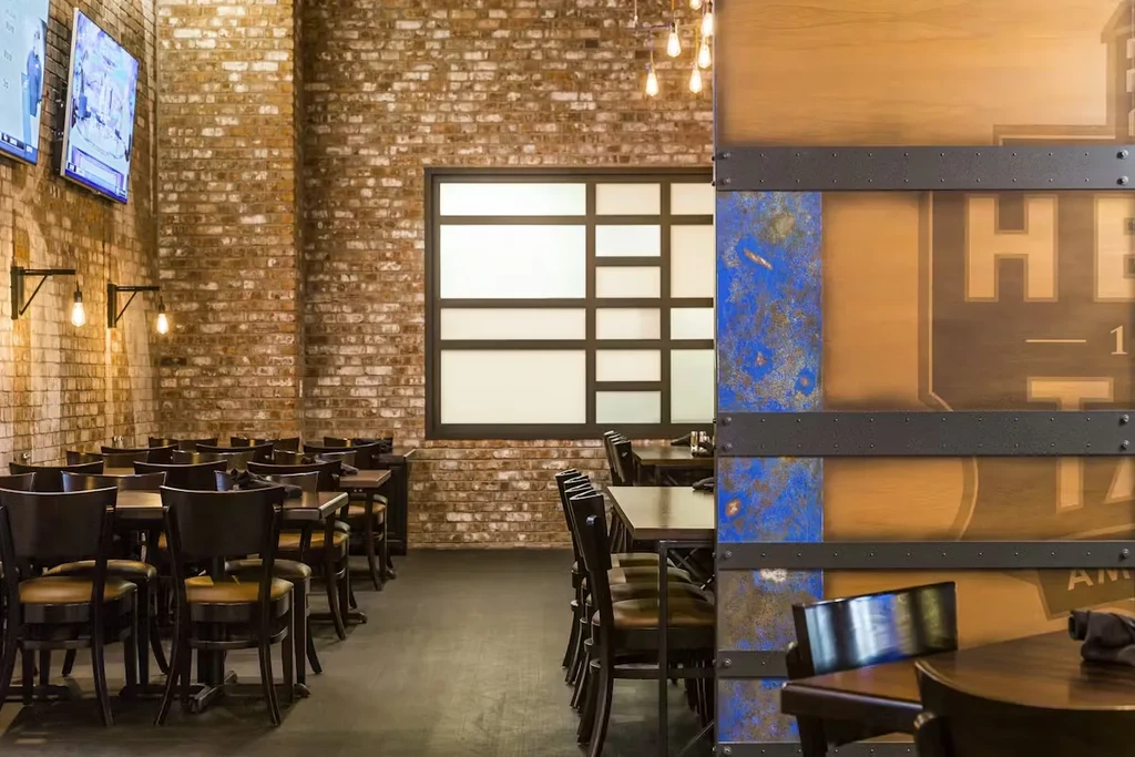 Casual restaurant interior with brick wall, TVs, tables, and metal-panelled partition.