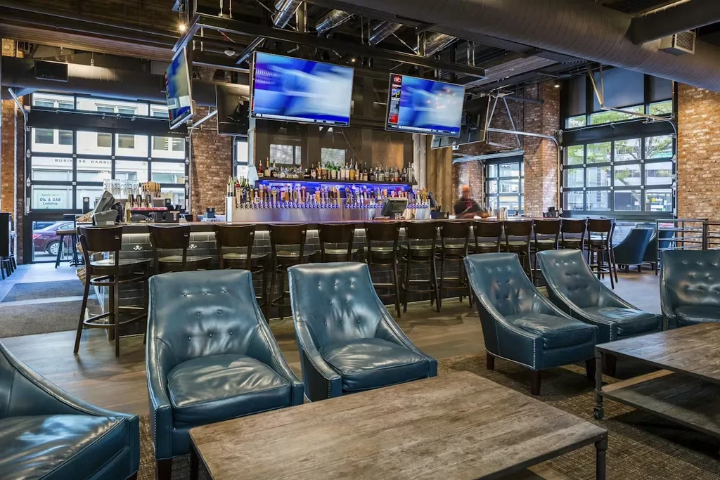Industrial bar interior with long bar, beer taps, TVs, and lounge seating.