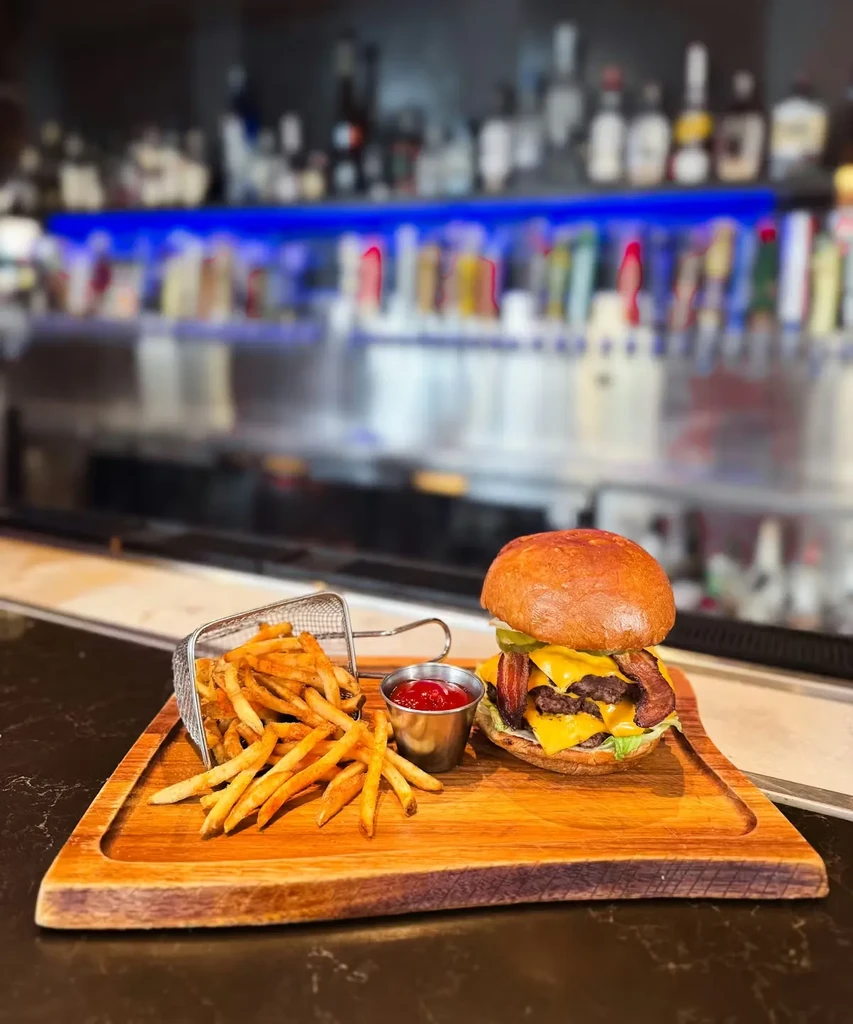 Gourmet double cheeseburger with fries, ketchup, and blurred bar background.