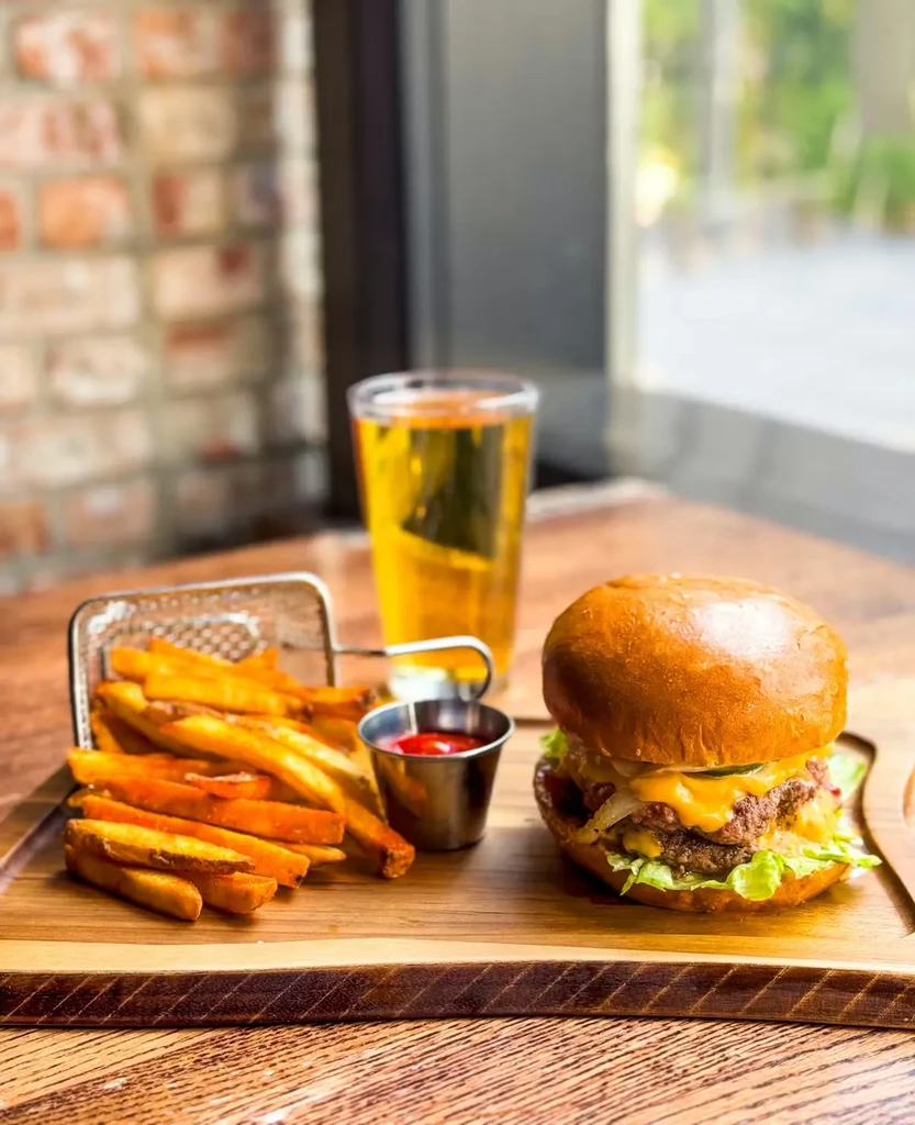 A double cheeseburger, fries, ketchup, and amber drink on a rustic board.
