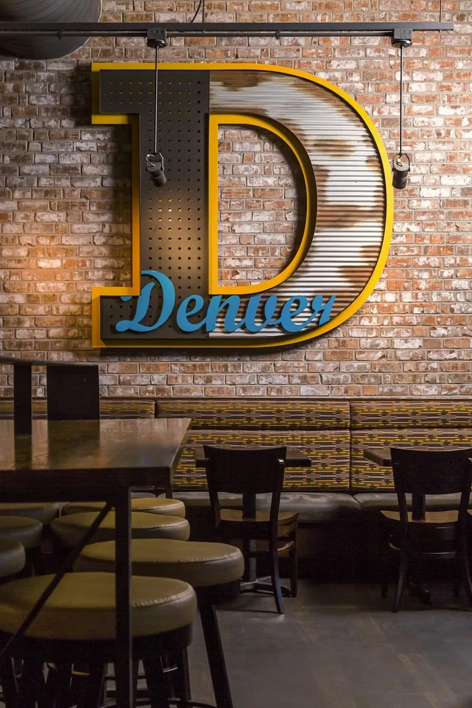 Stylized 'D' sign with 'Denver' on brick wall in a modern restaurant.