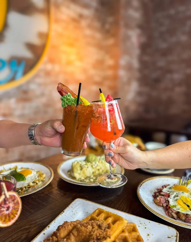 Hands toast Bloody Mary and fruity cocktails at a brunch table.