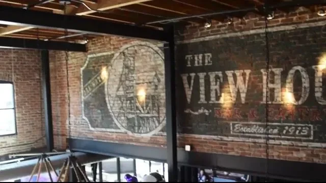 Industrial restaurant interior featuring "THE VIEW HOUSE" mural and architectural beams.