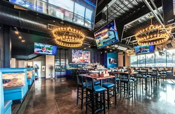 Modern sports bar interior with many TVs, blue booths, and snowy windows.