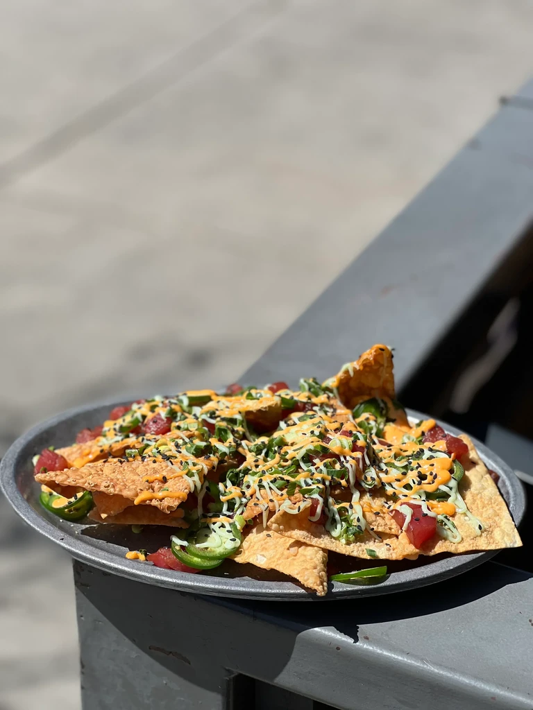 Gourmet nachos with red protein, jalapeños, green onions, and two sauces.