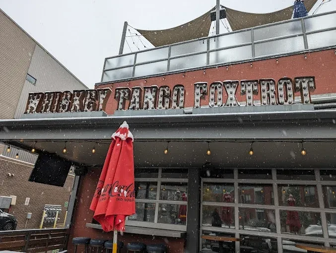 Snowy exterior of Whiskey Tango Foxtrot with illuminated sign and red umbrella.
