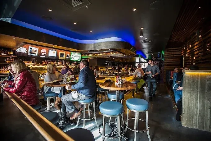 Modern, dimly lit bar interior with patrons and a blue light.