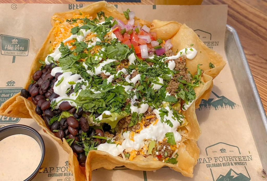 Taco salad in a fried tortilla bowl with beef, beans, and toppings.