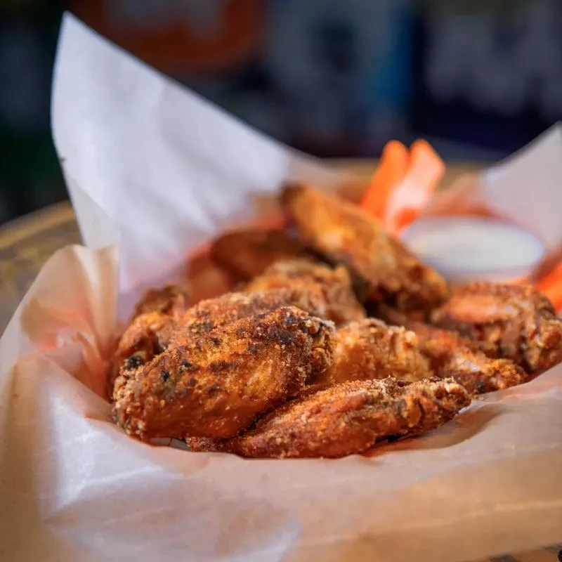 Basket of crispy, seasoned chicken wings with carrots and dipping sauce.