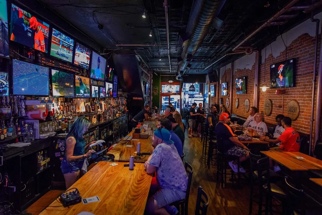 Bustling sports bar interior with multiple TVs, a long bar, and socializing patrons.