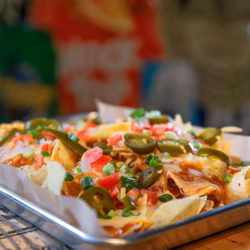 Close-up of vibrant nachos loaded with cheese, tomatoes, onions, scallions, jalapeños.