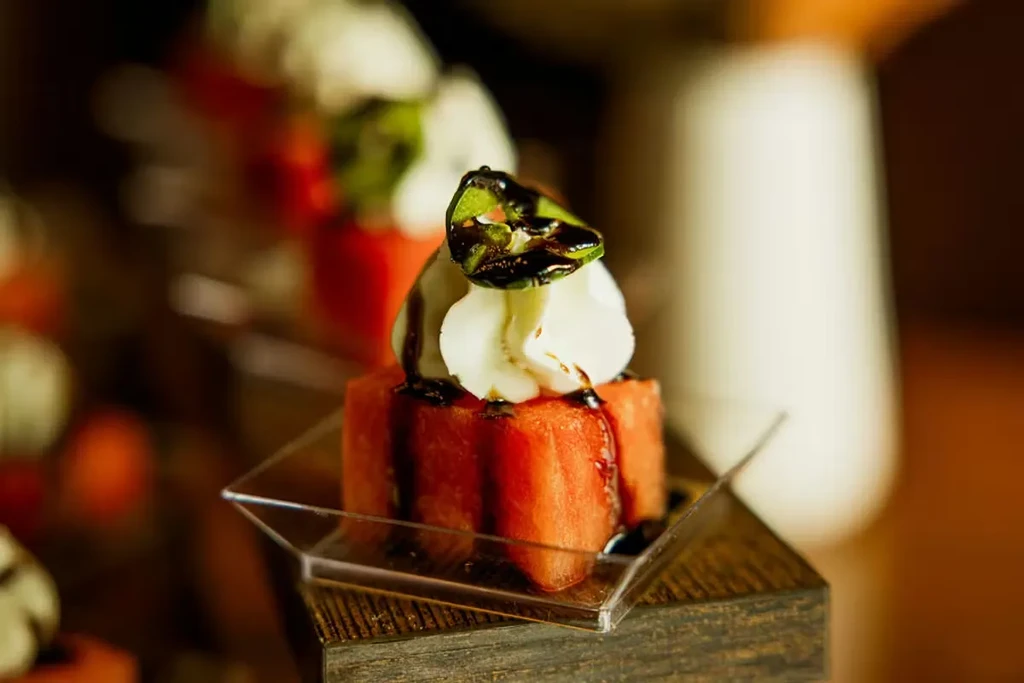Red watermelon cube with cream, green garnish, and balsamic glaze.