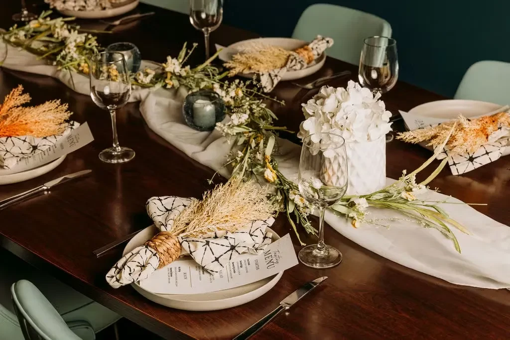 Long dark dining table with floral garland, candles, and individual place settings.