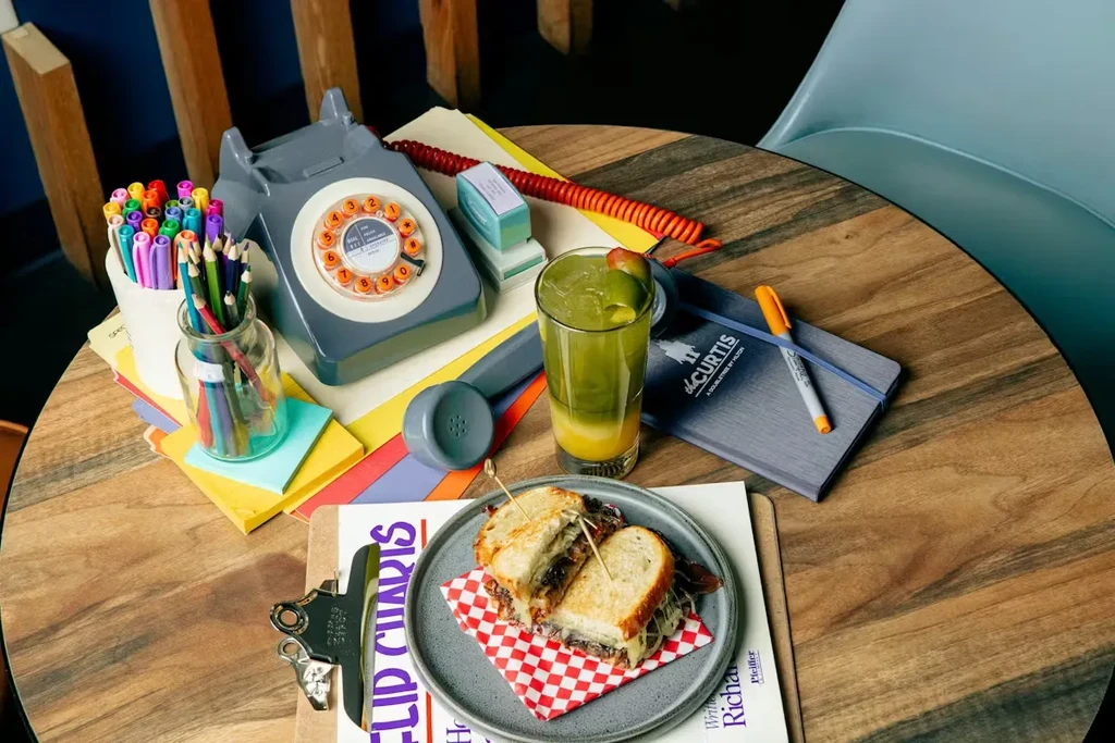 Sandwich and drink surrounded by office supplies on a wooden table.