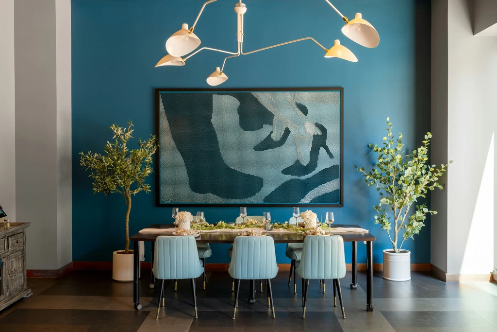 Modern dining room with blue chairs, set table, and pixelated wall art.