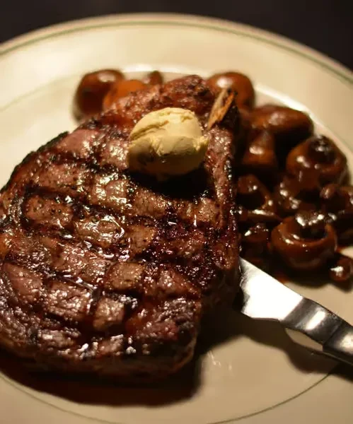 Well-grilled steak with melting herb butter, sautéed mushrooms, and steak knife.