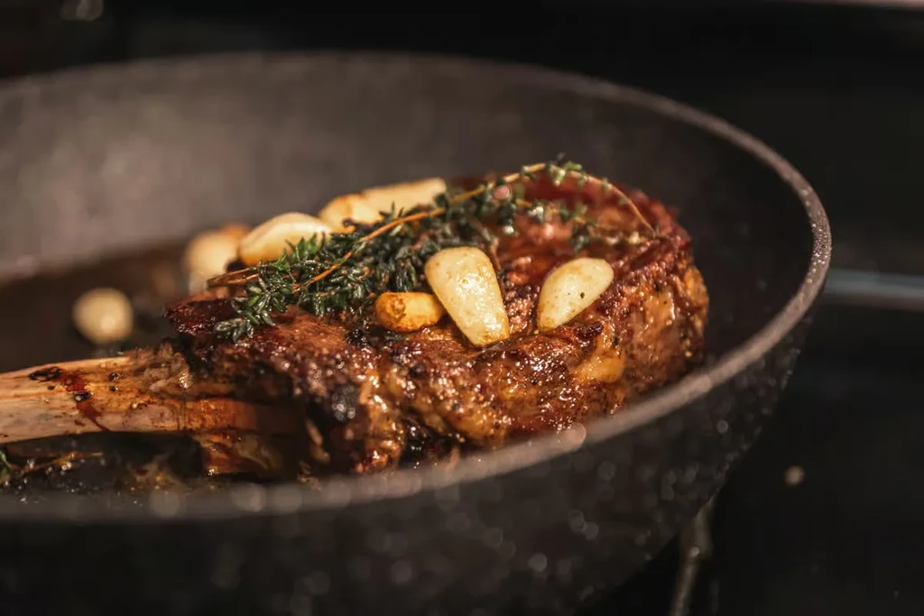 Seared bone-in steak cooking with garlic and thyme in a skillet.