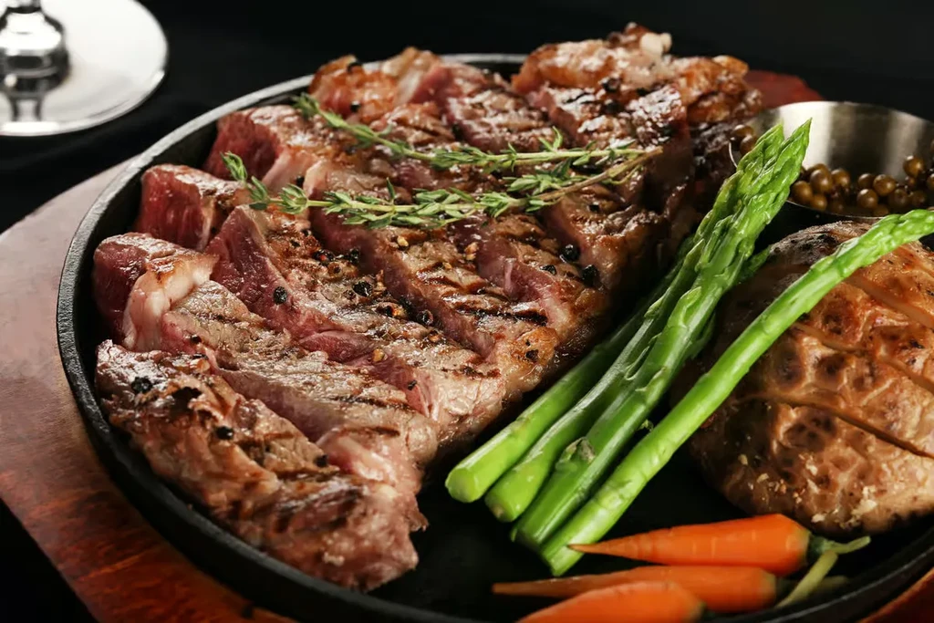 Sliced medium-rare steak with asparagus, potato, and carrots in skillet.