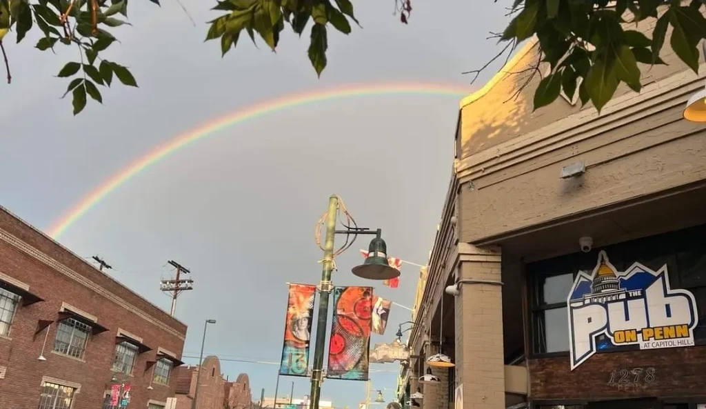 Rainbow arches over The Pub on Penn sign in an urban street.